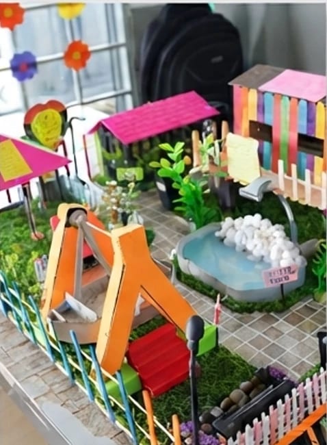 A student-built miniature playground with a swing, a pond and houses made of coloured craft sticks